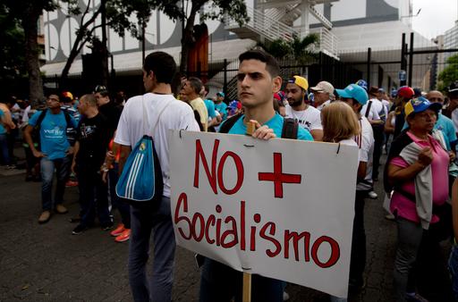 A young man holds poster with a message that reads in Spanish; "No more Socialism" as protesters gather for the taking of Caracas march in Caracas
