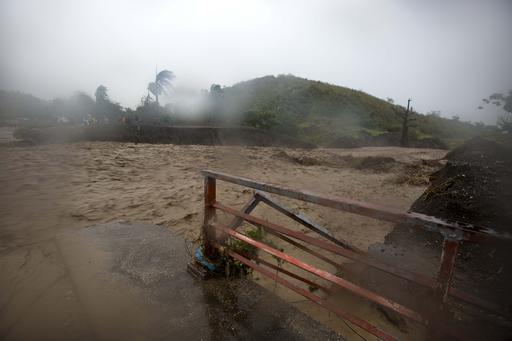 People watch from the other side of the La Digue river as water roars past the destroyed Petit Goave bridge
