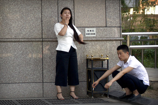 A man and a woman smoke cigarettes outside of an office building in Beijing