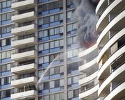 Firefighters on a lower balcony spray water upwards while trying to contain a fire at the Marco Polo apartments