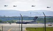 Helicopters fly above a military aircraft on the tarmac at the Stewart Air National Guard Base in Newburgh