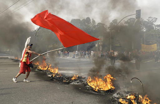 A demonstrator waves a red banner next to a burning barricade during a protest against Brazil's acting President Michel Temer