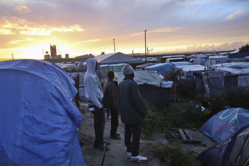 Migrants stand in a makeshift migrants camp near Calais