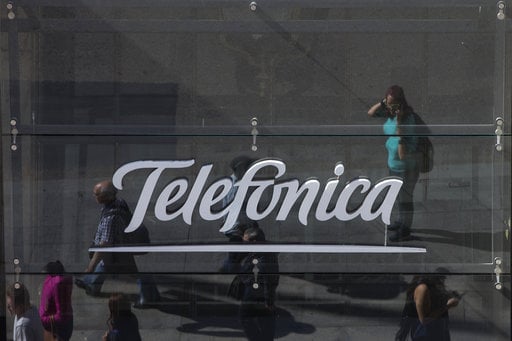 People are reflected in a glass sign of a Telefonica building in Madrid