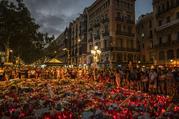 People stand next to candles and flowers placed on the ground