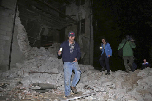 Residents walk past rubble in the village of Visso