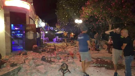 A man lies on the ground as other tourists stand outside a bar after an earthquake on the Greek island of Kos early Friday