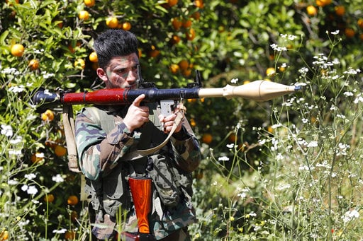 A Hezbollah fighter holds an RPG as he takes his position between orange trees
