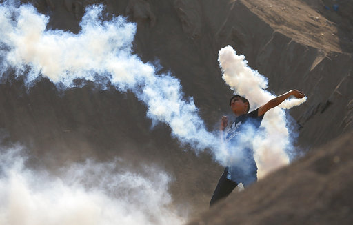 A Palestinian protester throws a teargas canister fired by Israeli soldiers back during clashes on the Israeli border with Gaza