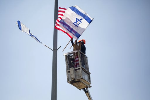 A worker hangs Israeli and American flags on a lamppost along a freeway leading to Jerusalem