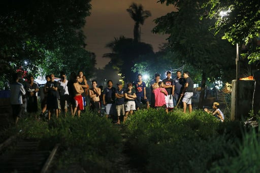 Residents are kept at a distance as police investigators examine the bodies of three suspects who were killed in an alleged "buy-bust" operation by the authorities in the continuing "War on Drugs" campaign of Philippine President Rodrigo Duterte before dawn Friday