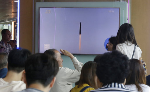 People watch a TV news program showing a file footage of a missile launched by North Korea