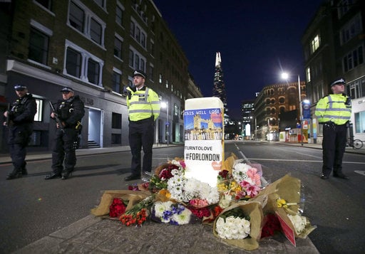 Police officers on duty stand next to floral tributes on Southwark Street in London