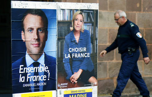 A municipal police officer walks near election campaign posters for French centrist presidential candidate Emmanuel Macron