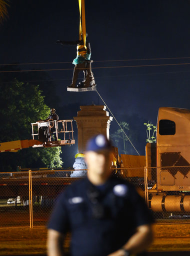 The figure of Jefferson Davis is removed from its base as police stand watch over demonstrators both for and against the removal of confederate era statues in New Orleans