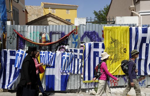 A Greek orthodox priest and tourists pass Greek flags in Athens