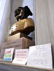 Signs stand in front of a bust of Nathan Bedford Forrest and a sweatshirt covers its face during a protest Monday