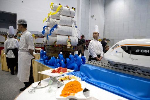 Chefs wait near a decorations depicting Chinese Admiral Zheng He who commanded expeditionary voyages across Asia and East Africa in the 15th century and a modern high speed rail at the Belt and Road Forum in Beijing