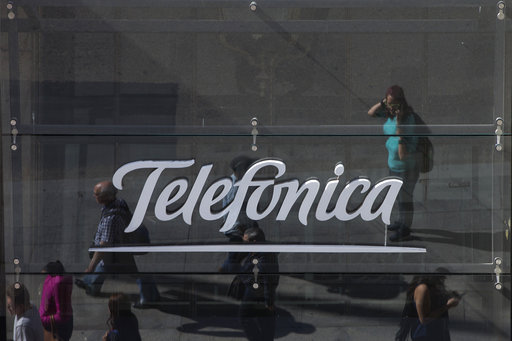 People are reflected in a glass sign of a Telefonica building in Madrid