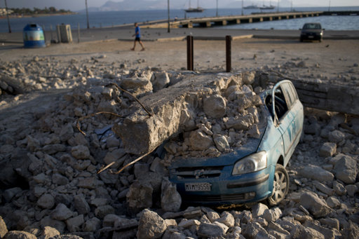 A man walks past a car crushed under rubble near the port of the Greek island of Kos on Saturday