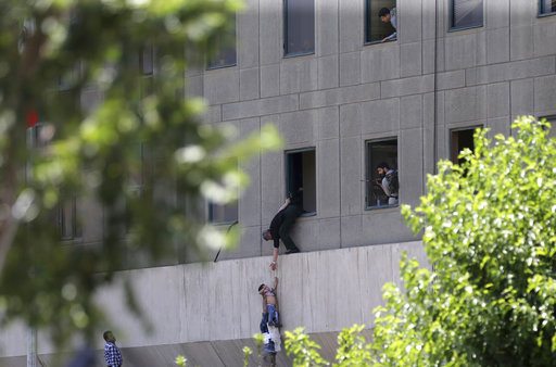 A man hands a child to a security guard from Iran's parliament building after an assault of several attackers
