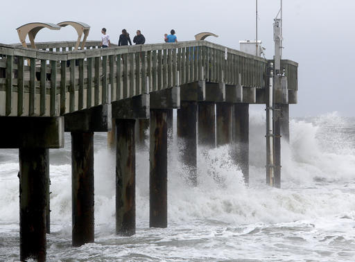 People stand on the pier as waves crash below as Hurricane Matthew approaches on Thursday