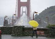 A woman walks in the rain at a vista point with the Golden Gate Bridge in the background Monday