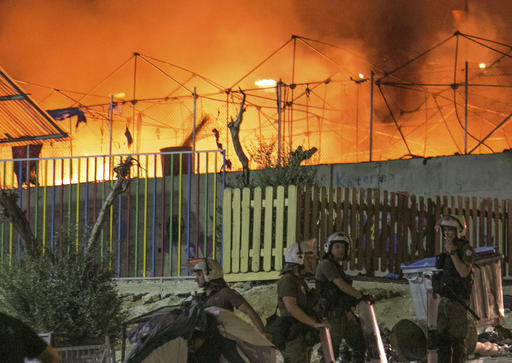 Riot police stand guard as a large fire burns inside the Moria refugee camp on the northeastern Greek island of Lesbos