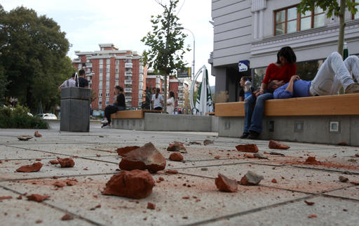 People sit outside buildings near fallen bricks