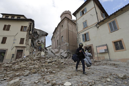 A resident carrying his belongings passes in front of the collapsed bell tower of the Santa Maria in Via church in the town of Camerino