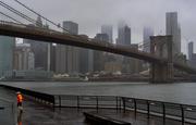 A runner moves along the Brooklyn shoreline of the East River as rain and clouds loom over lower Manhattan on the fifth anniversary of Superstorm Sandy Sunday