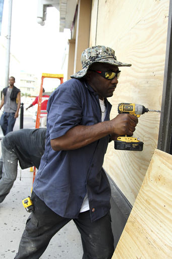 Yorick Bain uses a drill to secure plywood over the windows of a Dunkin Donuts store in downtown Nassau