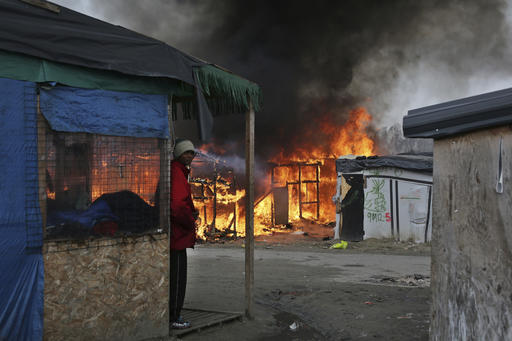 A man stands next to a burning tent as fires were started in the makeshift migrant camp known as "the jungle" near Calais