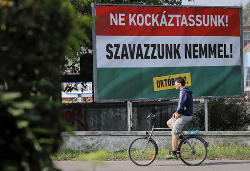 A man rides a bicycle by a poster that reads in Hungarian "Lets not risk it! Lets vote no! October 2"