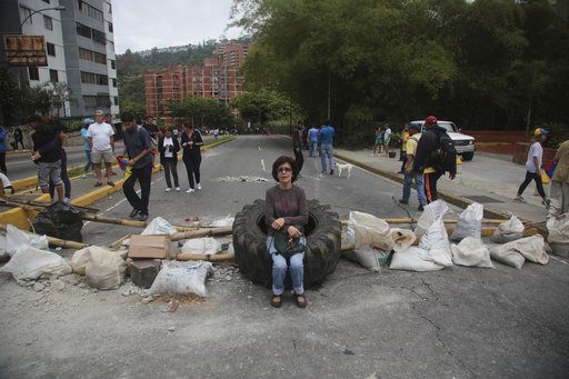A woman rests on a tire at a roadblock set up by residents outside her home in El Hatillo's municipality near Caracas