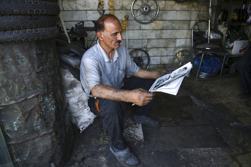 A motorcycle repairman reads a newspaper at his shop near Iran's parliament building in Tehran