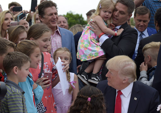 President Donald Trump talks with children as be sits down to write a letter to a service member during the annual White House Easter Egg Roll on the South Lawn of the White House in Washington