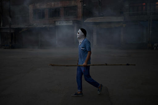 A Kashmiri Muslim protester holds a bamboo stick as stands in tear gas smoke during a protest after funeral prayers in absentia for Pakistani soldiers killed in cross border firing in Srinagar