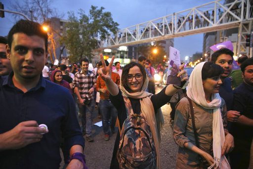 A supporter of the Iranian President Hassan Rouhani flashes a victory sign while holding his portrait in a street celebration after he won the Friday's presidential election