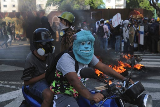An anti-government protester wearing a mask depicting the Monster Inc. character Sulley drives a motorbike through a barricade set up by fellow protesters