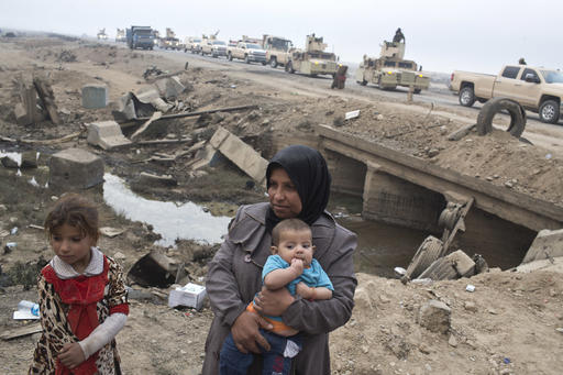 Internally displaced persons stand at a checkpoint as an Iraqi army convoy passes by in Qayyarah
