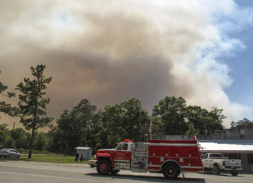 A fire truck passes as a plume of smoke rising from a wildfire burning