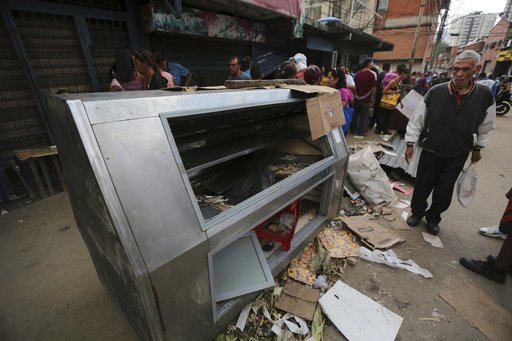 A pedestrian stands next to a refrigerator destroyed during looting the night before in the Valle neighborhood in Caracas