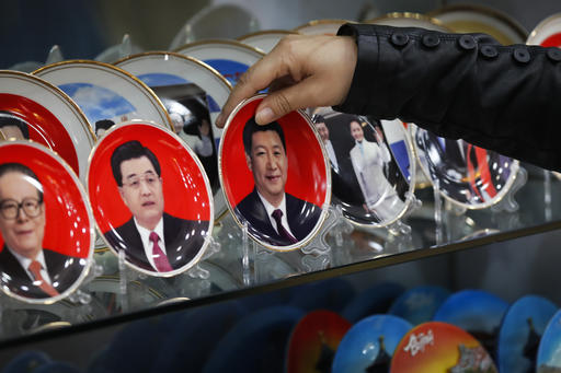 A worker takes a porcelain plate bearing an image of Chinese President Xi Jinping for a customer which on display together with previous leaders Jiang Zemin