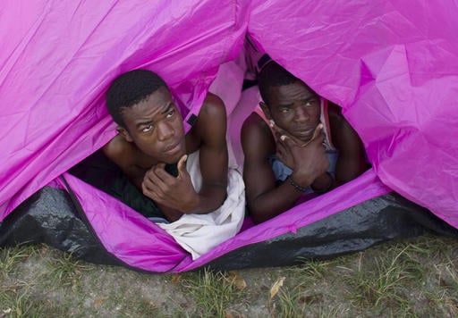 Young men whose home was destroyed by Hurricane Matthew peer out of a tent as they awake for the day in the courtyard of a school where they have sought shelter