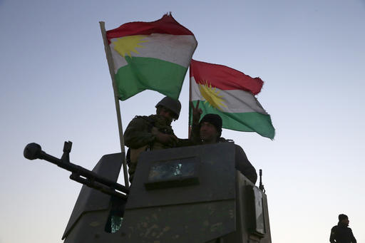 Kurdish Peshmerga fighters stand on top of a military vehicle as they advance towards villages surrounding Mosul