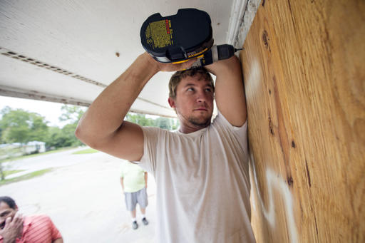 Alec Manning drills holes into plywood to cover the windows of a business during storm preparations for Hurricane Matthew