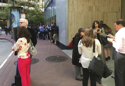 People stand outside their office building in the Financial District after a power outage Friday