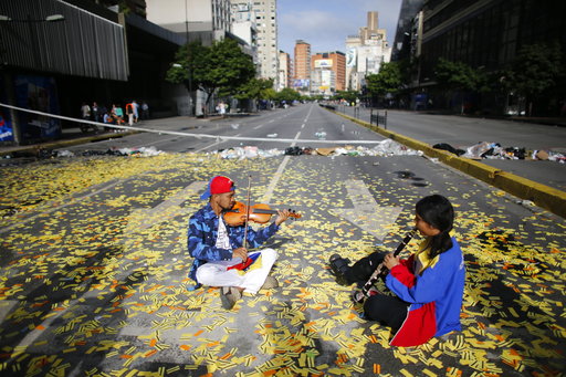 Musicians play their instruments as they sit in the middle of a road littered with metro tickets at a roadblock set up by anti-government protesters in Caracas