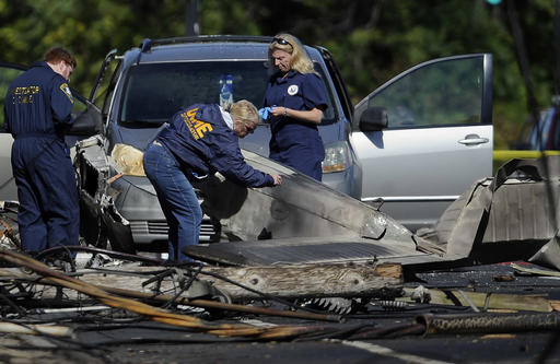 Investigators look at the remains of a small plane along Main St